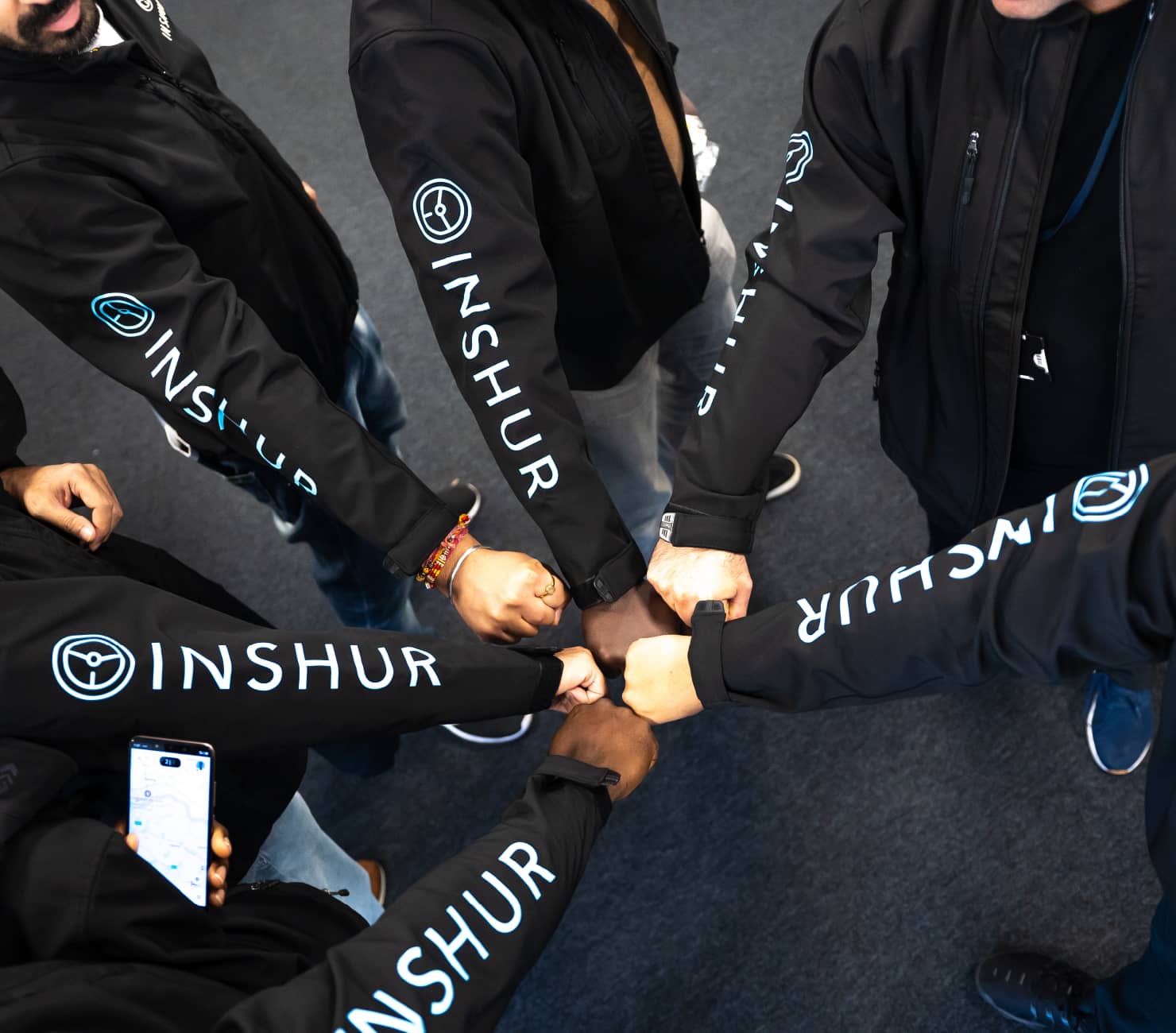 A circle of INSHUR employees in branded hoodies bumping fists