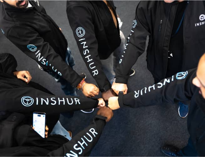 A circle of INSHUR employees in branded hoodies bumping fists