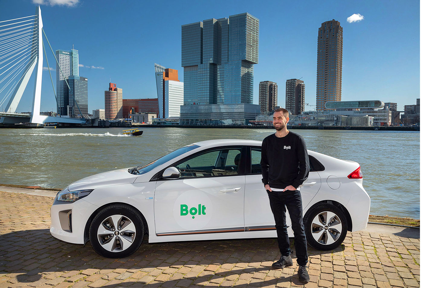 Bolt driver standing next to a white car with the city skyline in the background