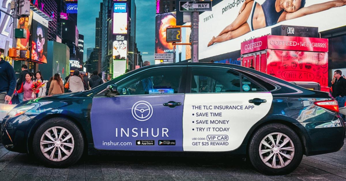 A black, INSHUR-branded car parked next to a busy city street